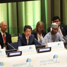 Group of individuals sat at white table. There is a large green curtain behind.