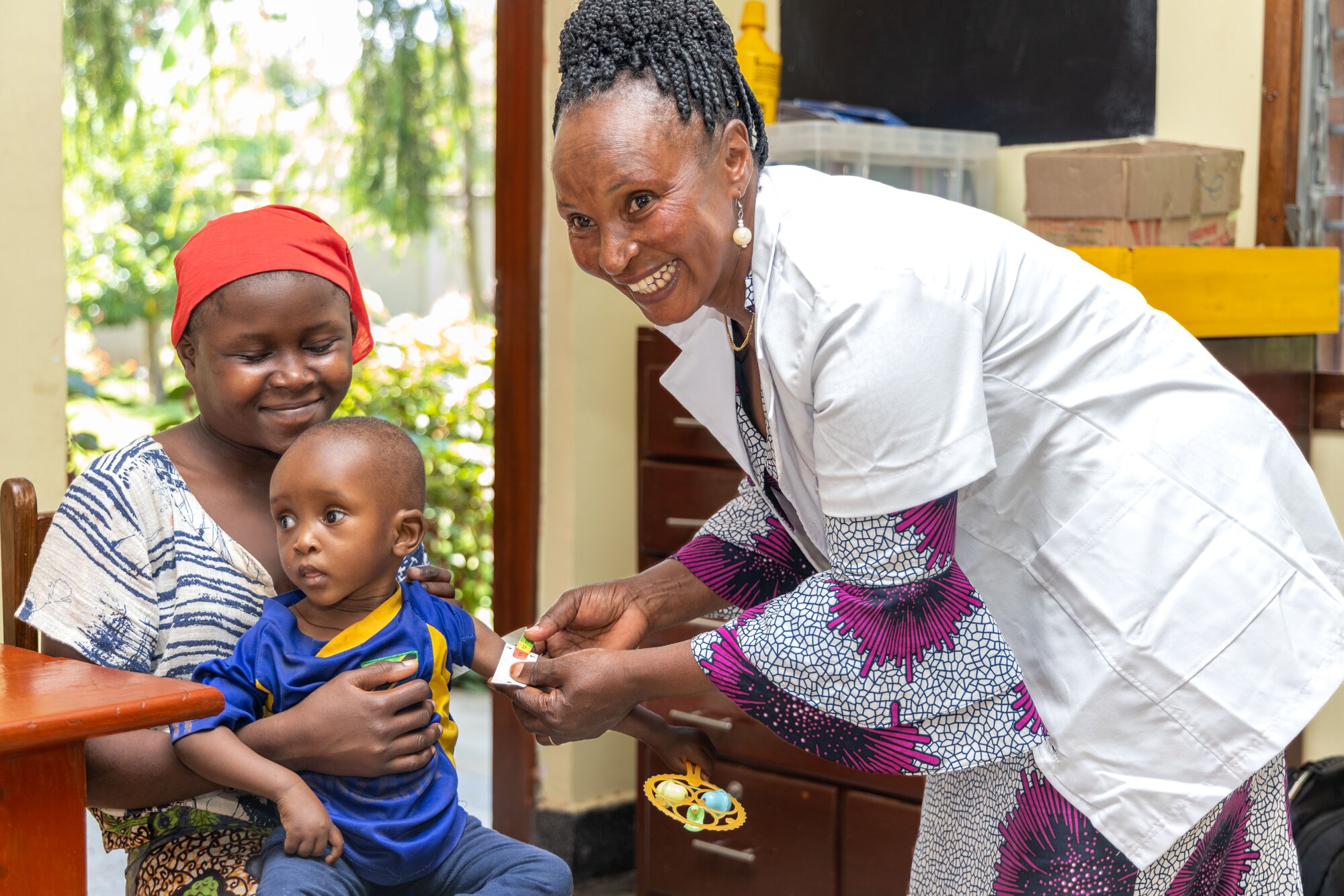 Mother holding her two-year-old daughter with cerebral palsy in a community clinic in Tanzania. A health care worker is attending to them, determining her nutritional status.