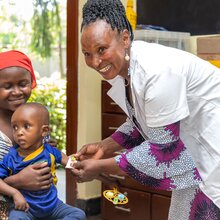 Mother holding her two-year-old daughter with cerebral palsy in a community clinic in Tanzania. A health care worker is attending to them, determining her nutritional status.